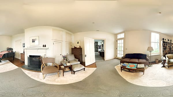 A bright living room with a grand piano, a sofa and coffee table, bookshelves and several windows