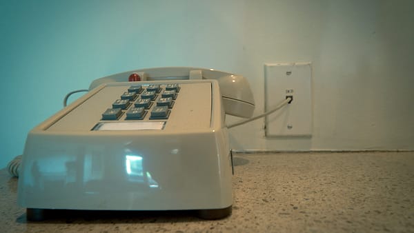 An old landline telephone mounted on the wall of a hotel, its handset resting in the cradle