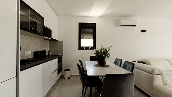 A domestic kitchen and dining area with white cabinets, a table and chairs, and sunlight from one window