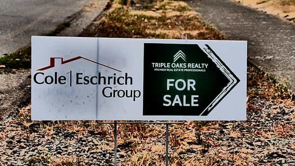 A real estate agent's For Sale sign standing on the grass in front of a property in Eugene, Oregon