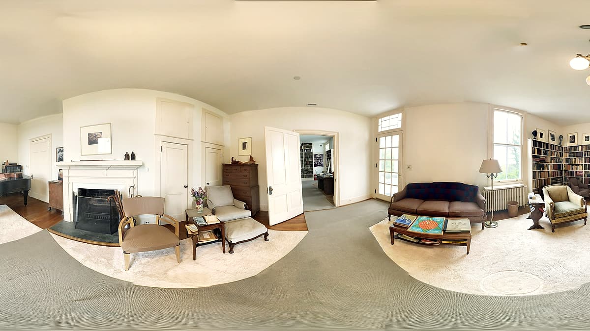 A bright living room with a grand piano, a sofa and coffee table, bookshelves and several windows