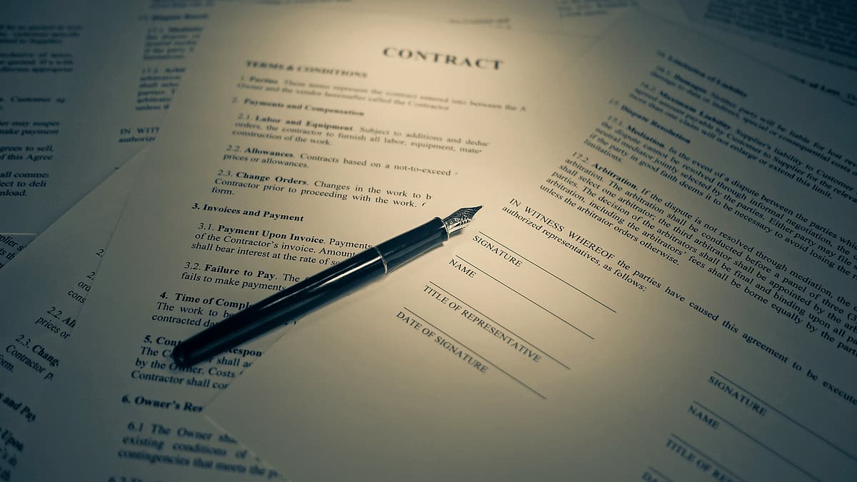 A printed contract lying on a desk in warm light, with a pen resting across the signature block