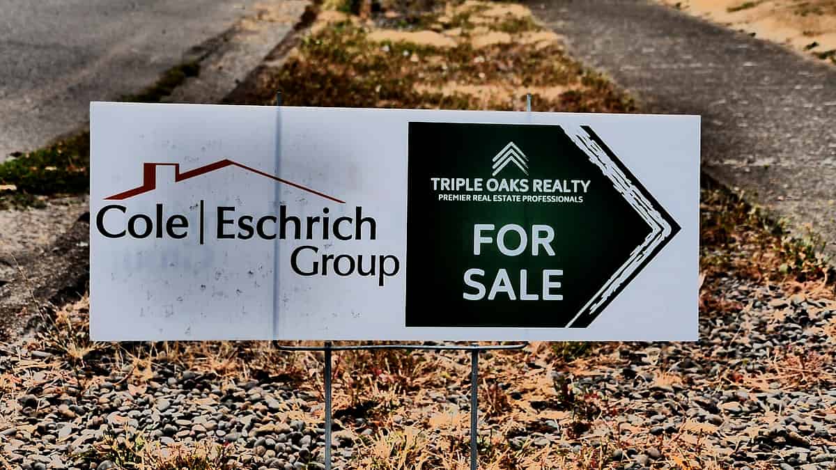 A real estate agent's For Sale sign standing on the grass in front of a property in Eugene, Oregon
